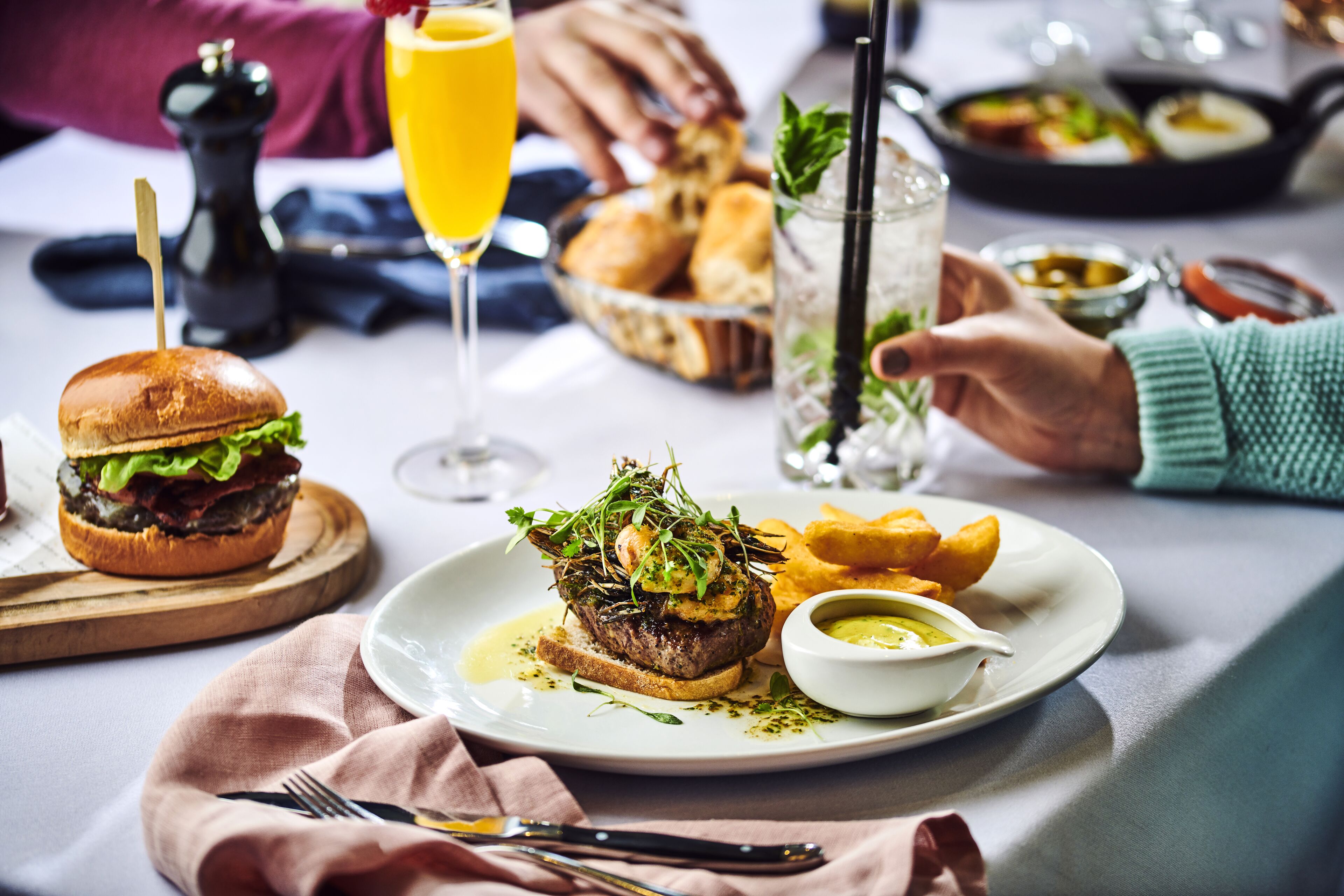 A dining table with a plate of food, including a burger and fries, a glass of orange juice, and a drink with a straw.