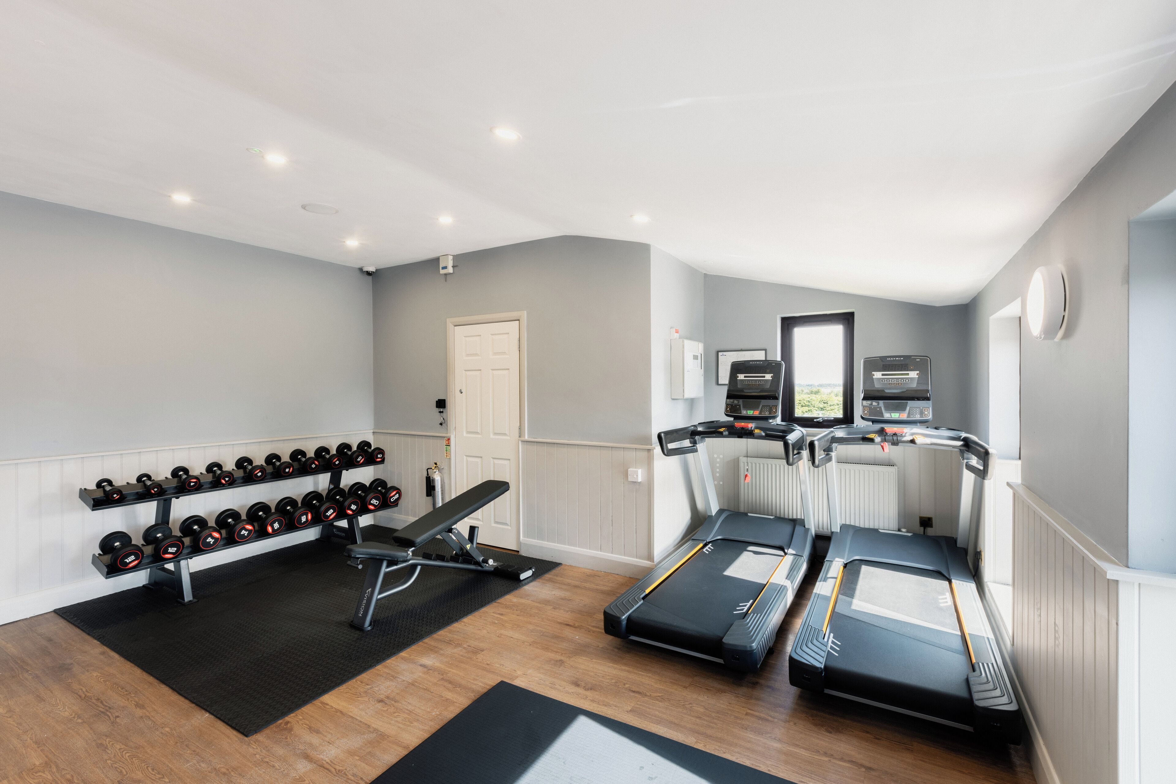 Un gimnasio en casa con cintas de correr, mancuernas y una banca.