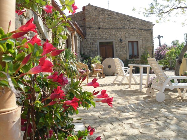 A stone building with a door and windows, surrounded by potted plants and outdoor furniture.