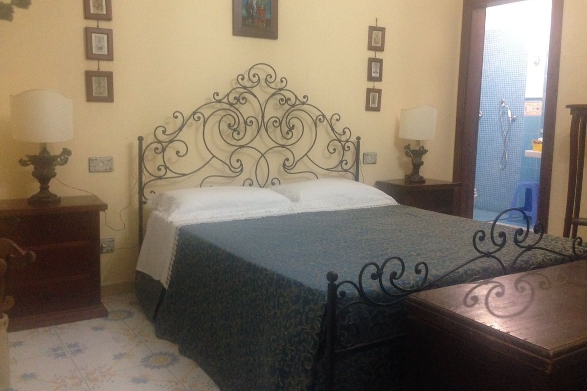 Une chambre à coucher comprenant un lit, deux tables de chevet, une commode, une décoration murale et une porte donnant accès à une salle de bain.