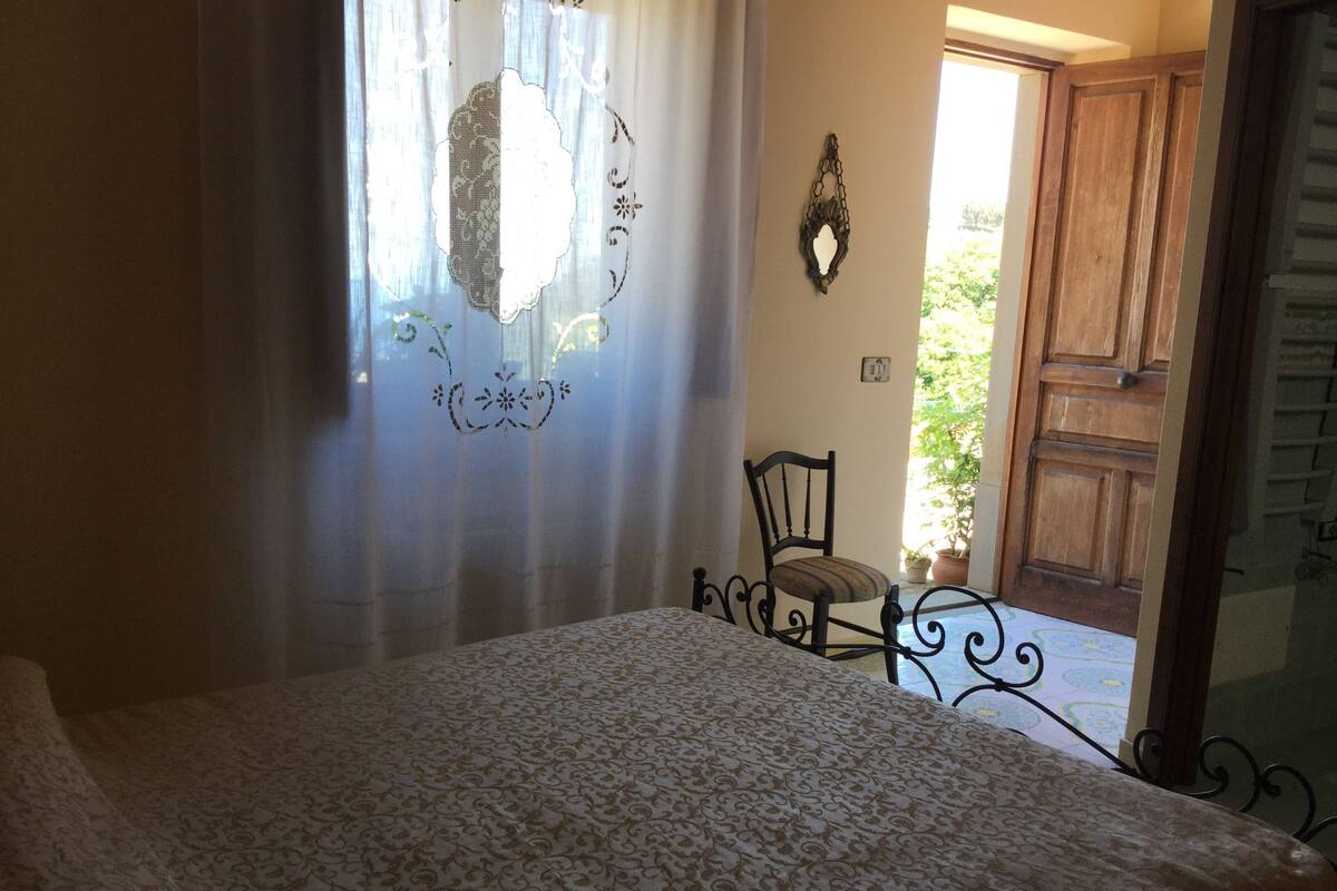 Une chambre à coucher comprenant un lit, une chaise, une décoration murale et une porte en bois donnant sur l’extérieur.