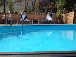 A swimming pool with two striped lounge chairs and a small table.
