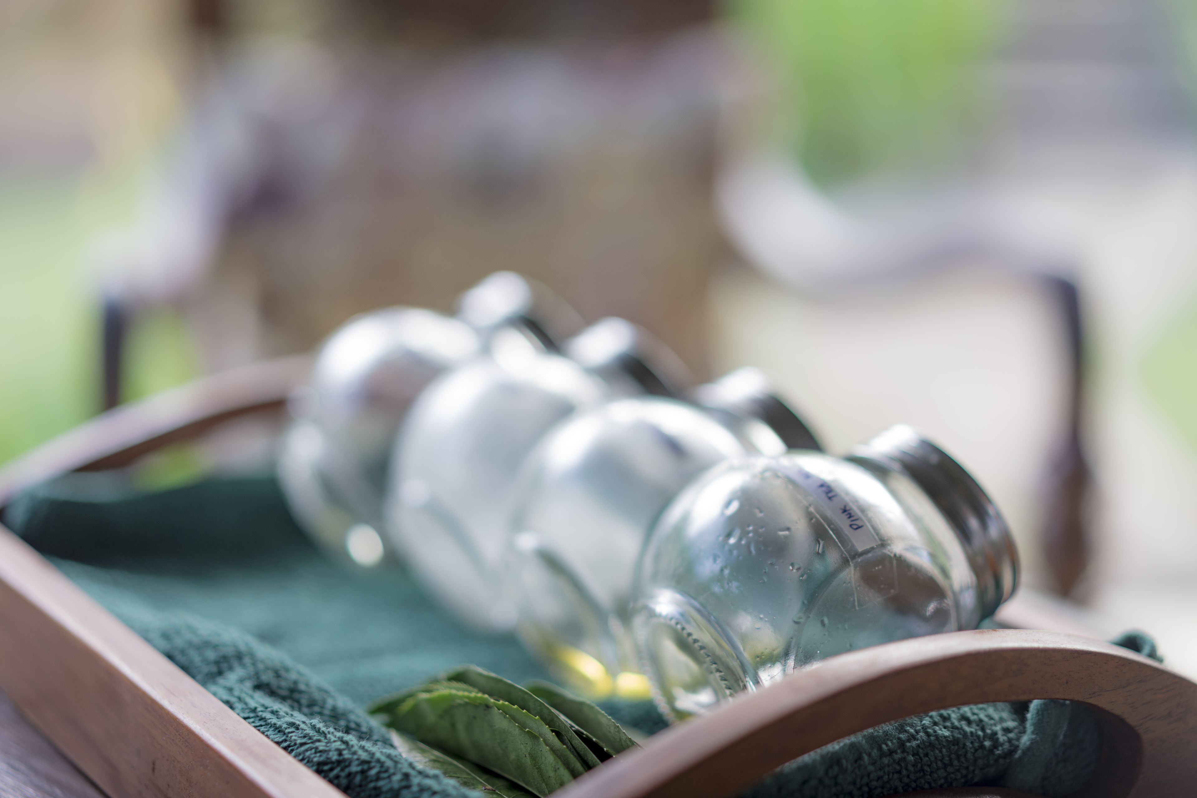 A wooden tray with a green cloth, holding several clear glass bottles with labels, and a green cloth napkin.