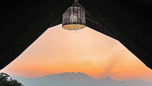 A balcony with two chairs and a table, overlooking a mountain range at sunset.