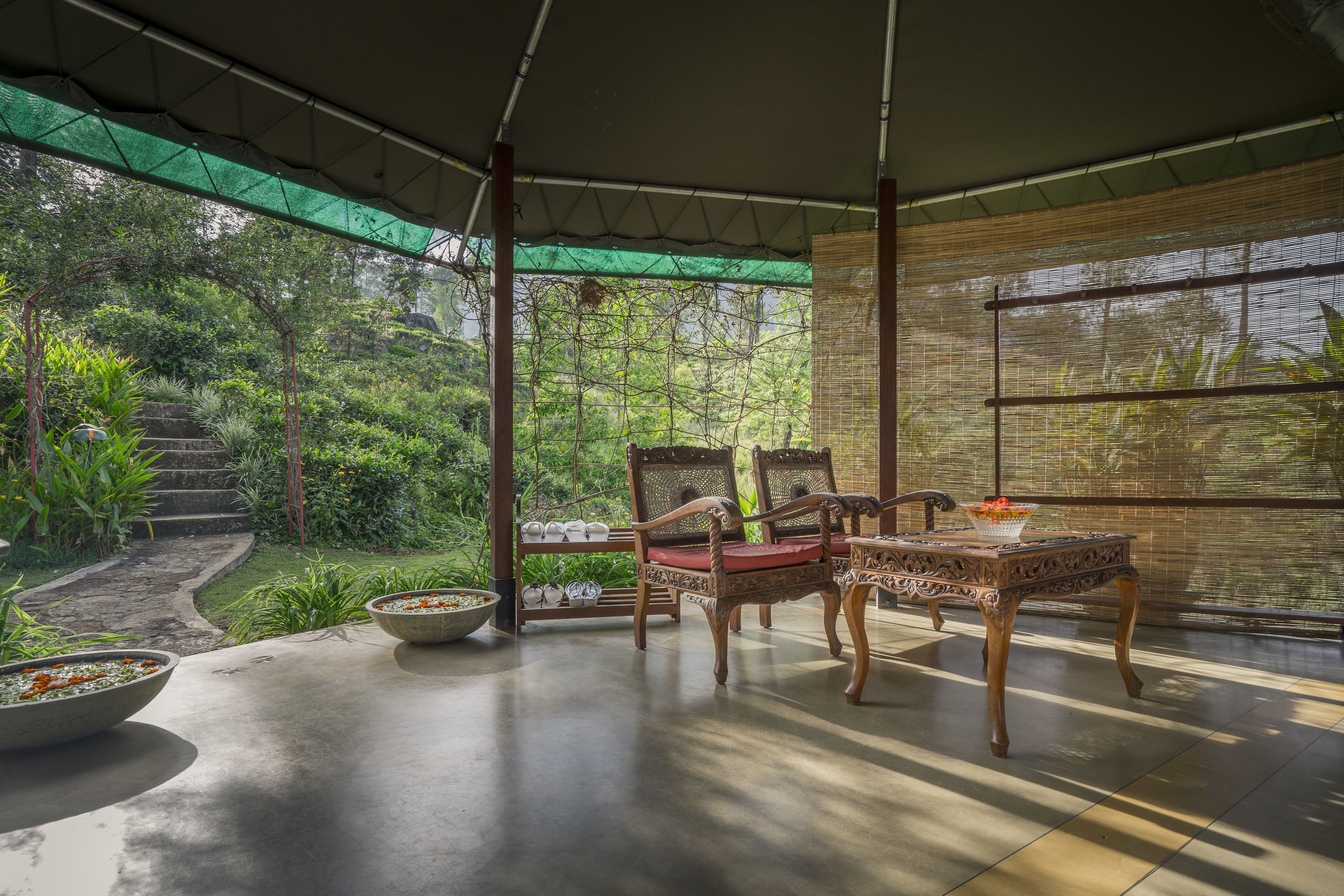 An outdoor seating area with a table and chairs, surrounded by lush greenery and a view of a garden.
