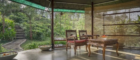 An outdoor seating area with a table and chairs, surrounded by lush greenery and a view of a garden.