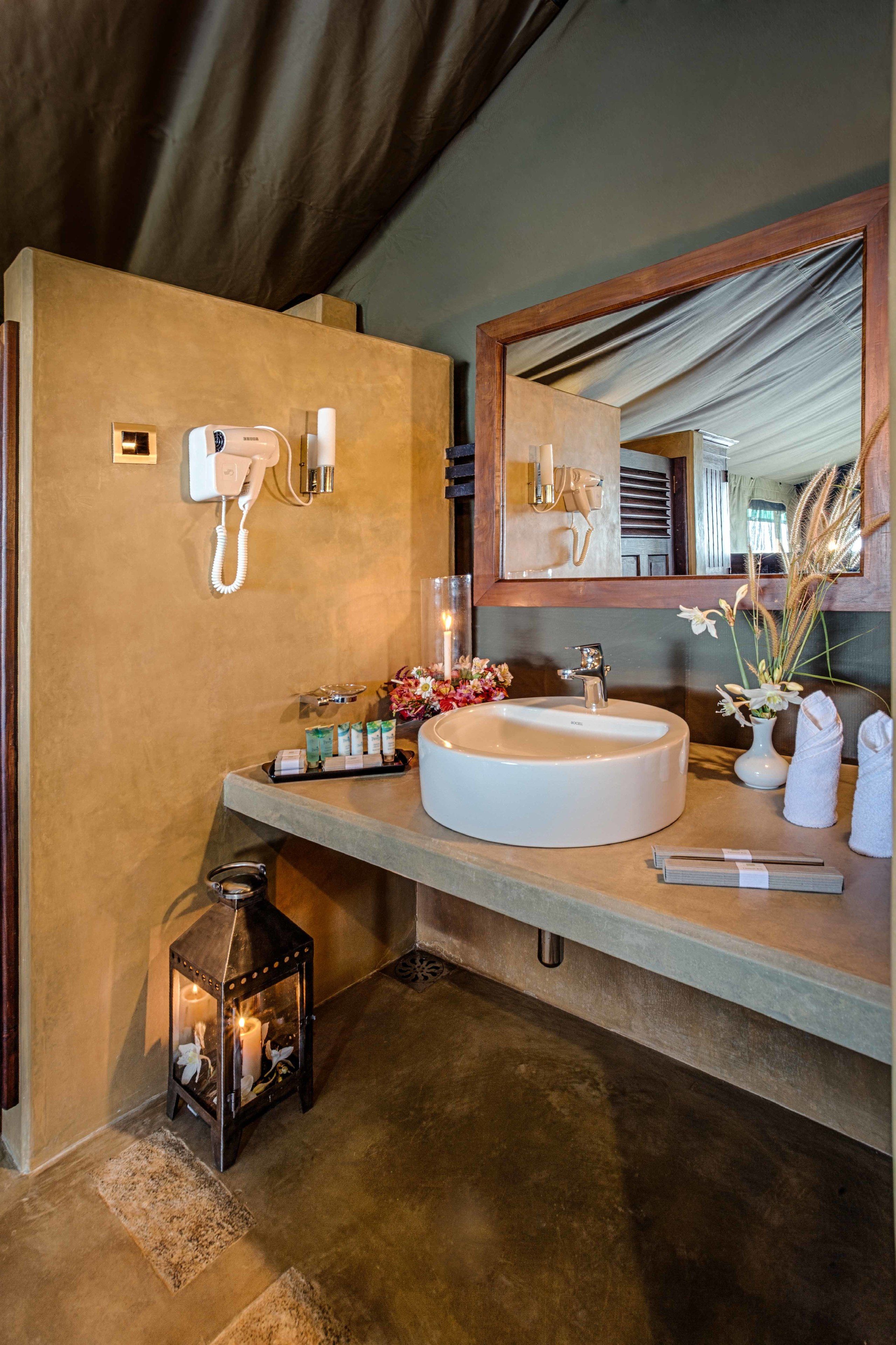 A bathroom with a round sink, a mirror, a towel rack, and a small lantern.
