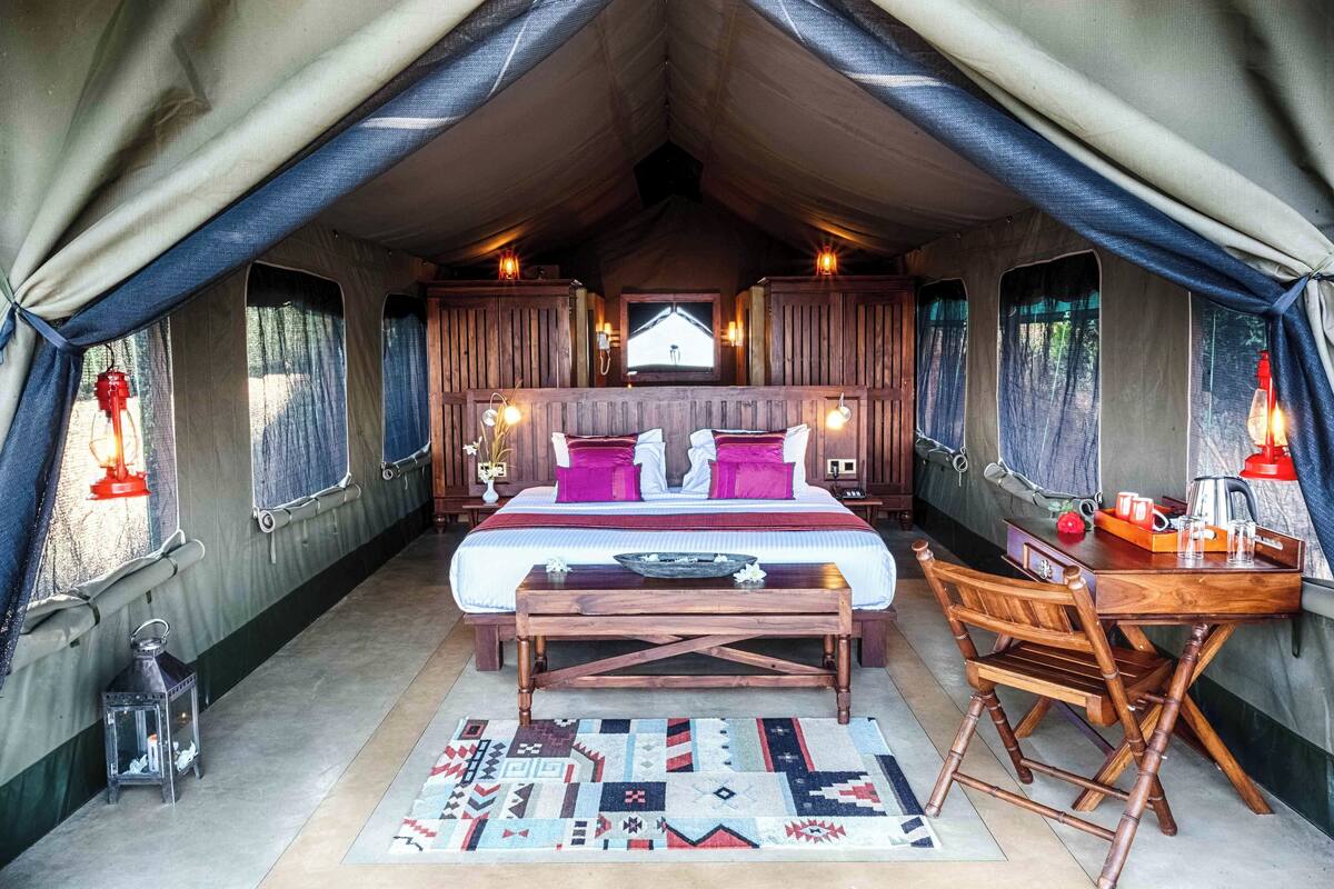 Une pièce aménagée avec une tente, un lit, un bureau en bois et une chaise.
