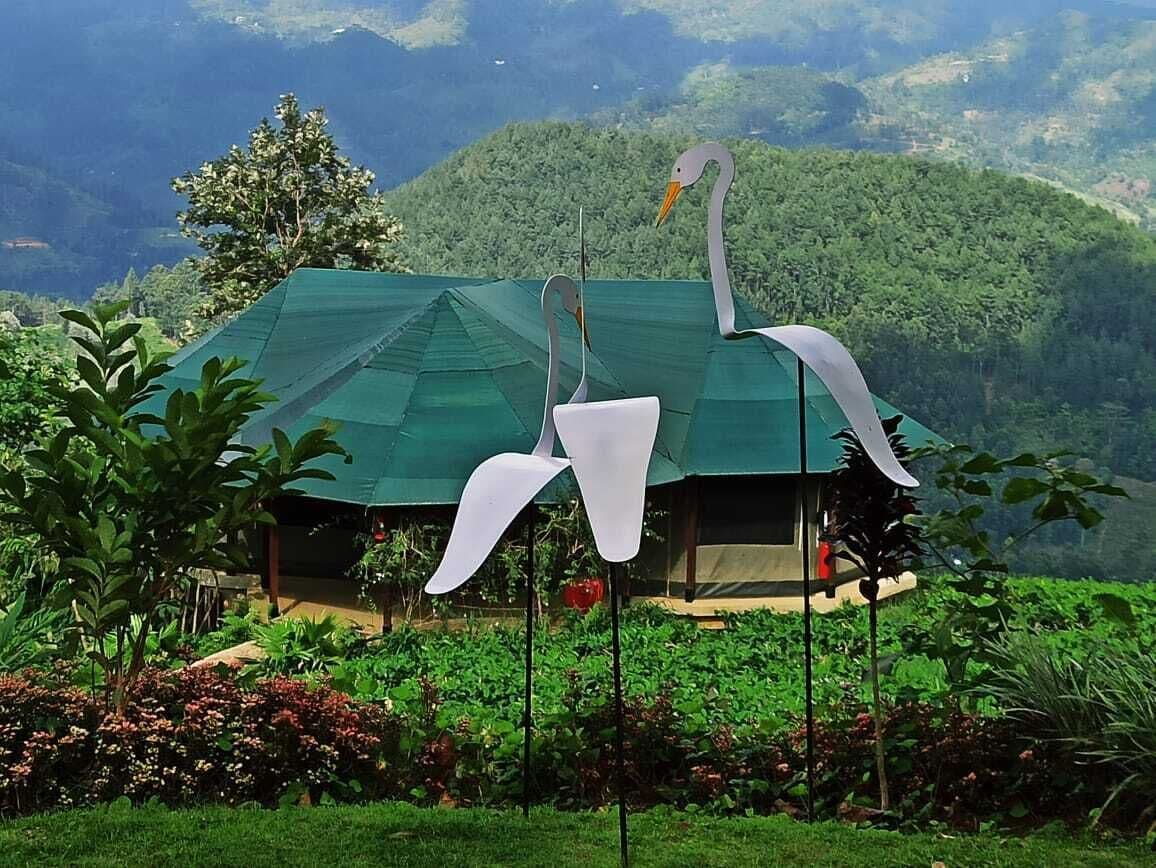 A green-roofed building surrounded by lush greenery and a mountainous backdrop.