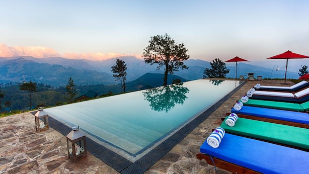 A infinity pool with a mountain view, stone flooring, and lounge chairs with umbrellas.