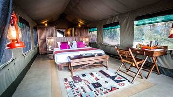 A tented room with a bed, wooden furniture, a rug, and a view of the outdoors.