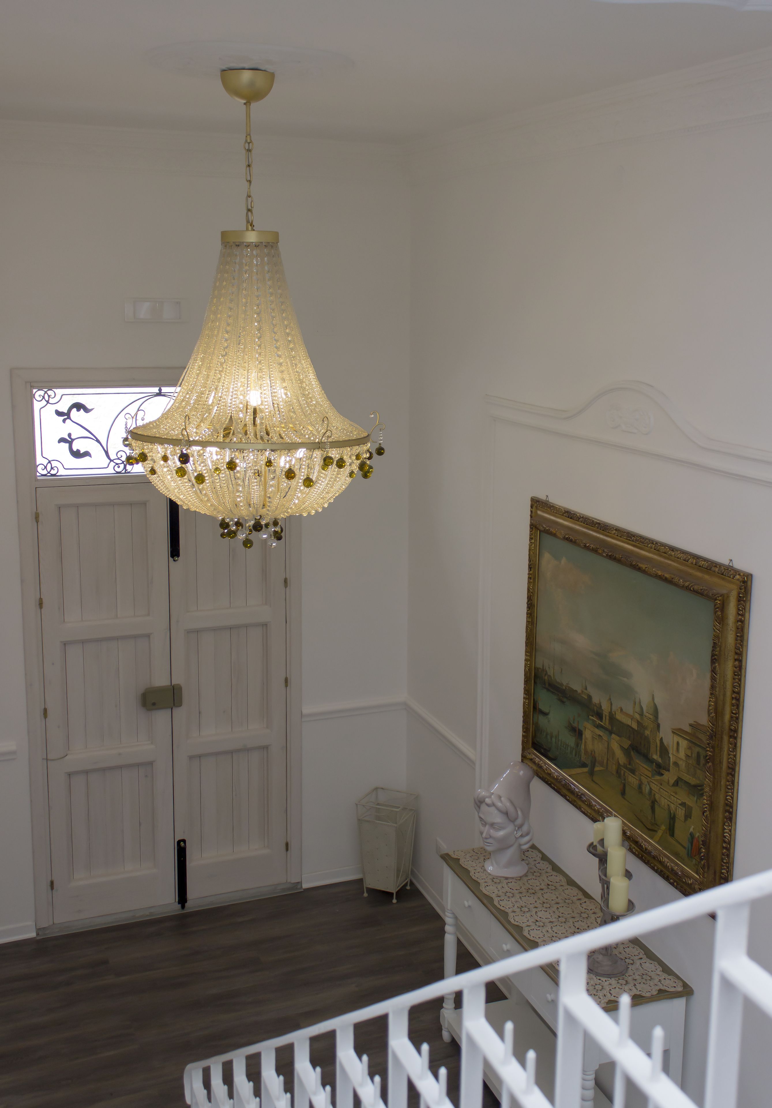 Un pasillo con una puerta y una escalera blancos, y un candelabro.