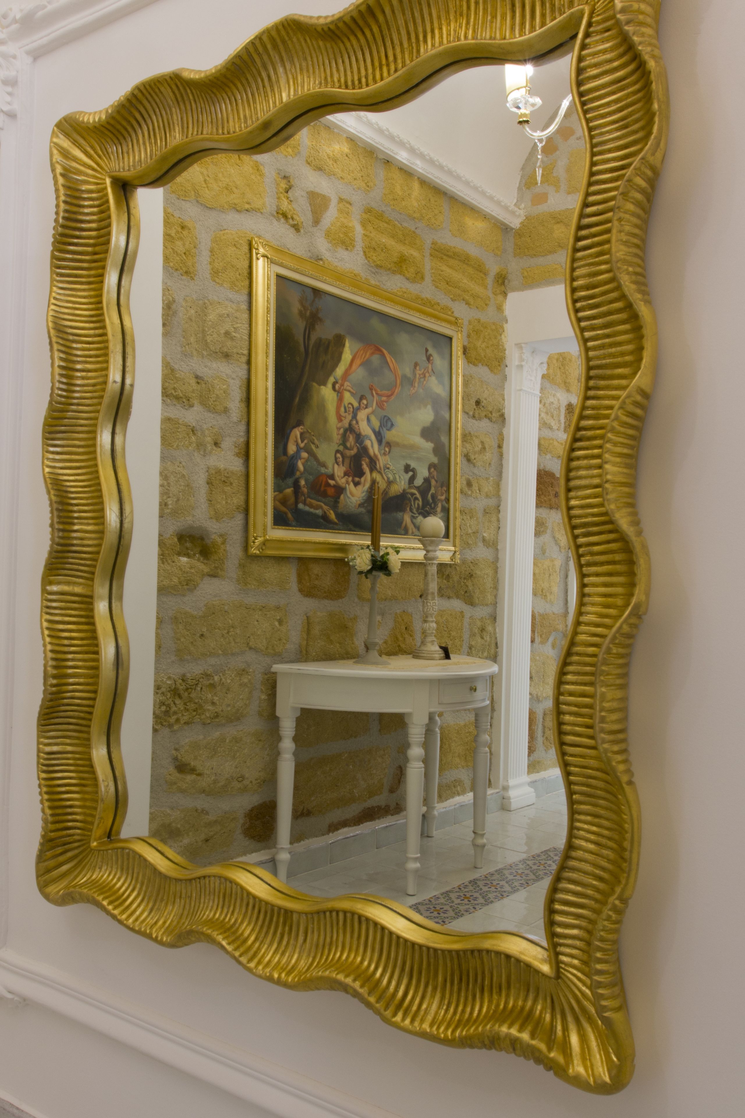 A room with a gold-framed mirror, a white console table, and a painting on the wall.