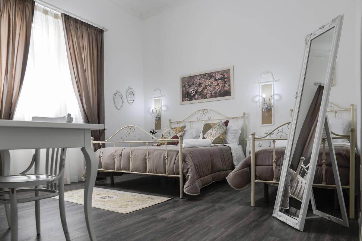 A bedroom with a bed, bedside tables, a chair, a mirror, and a painting on the wall.