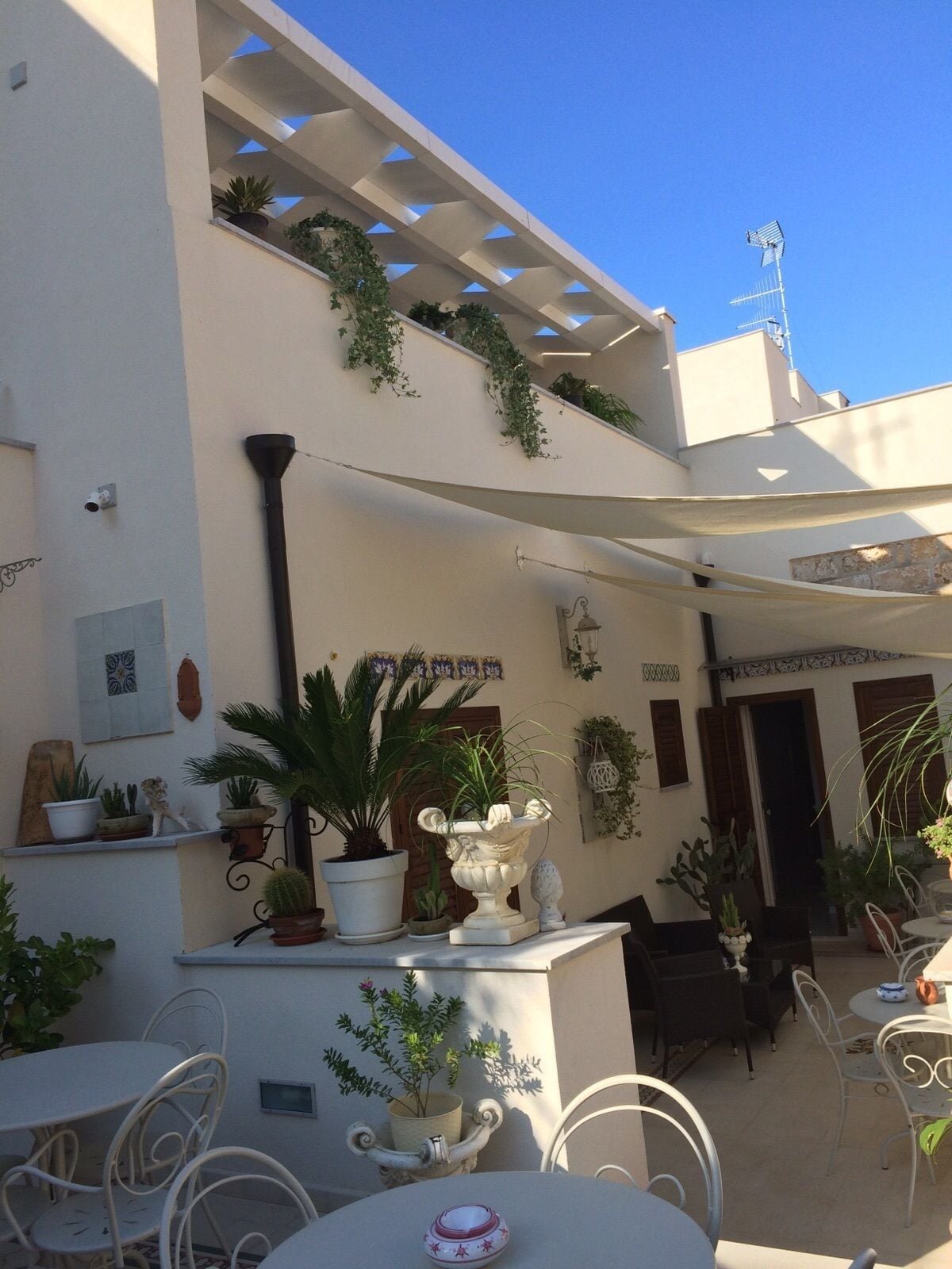 Un patio con mobiliario exterior, plantas en macetas y una pérgola.