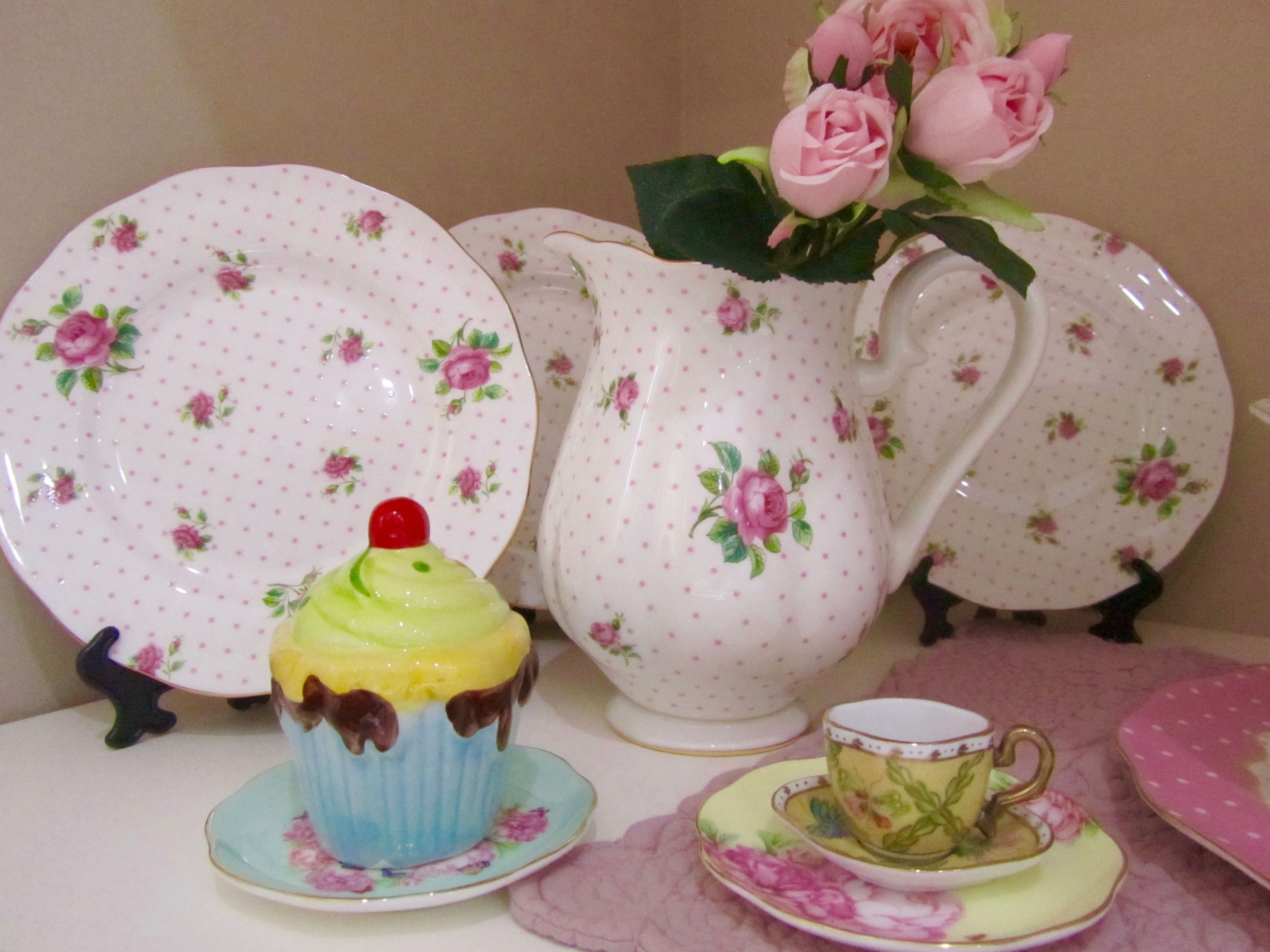Un tavolo con piatti a motivi floreali, una brocca, una cupcake e una tazza da tè.