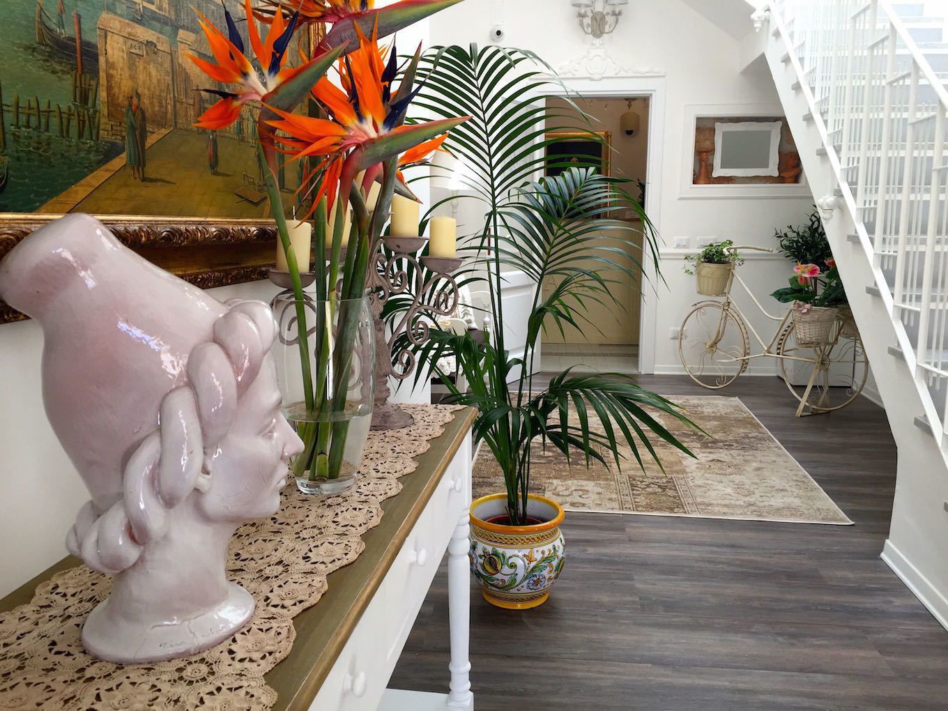 A hallway with a white staircase, a large painting, and various potted plants.