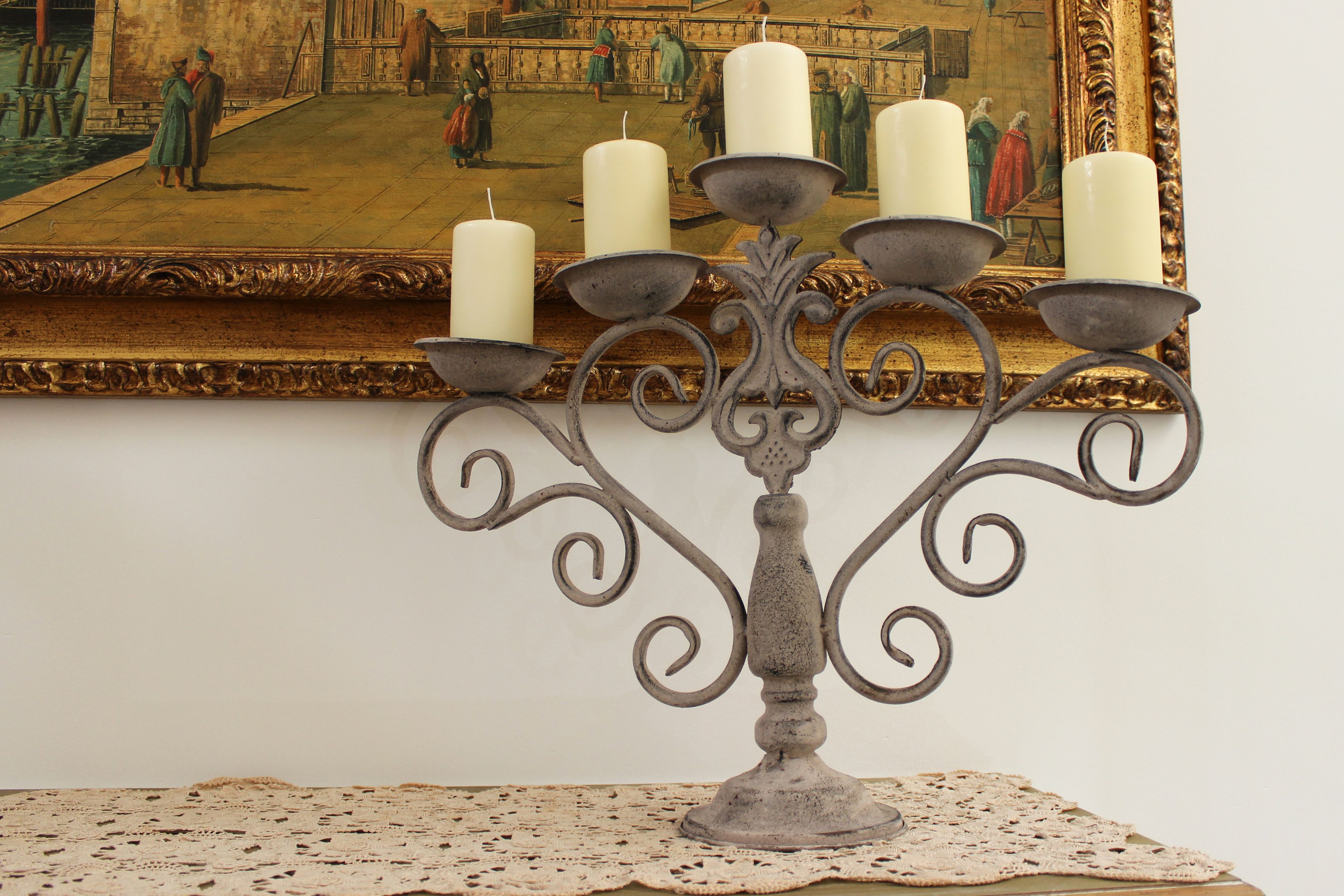 A candle holder with multiple candles on a table, placed in front of a framed painting.
