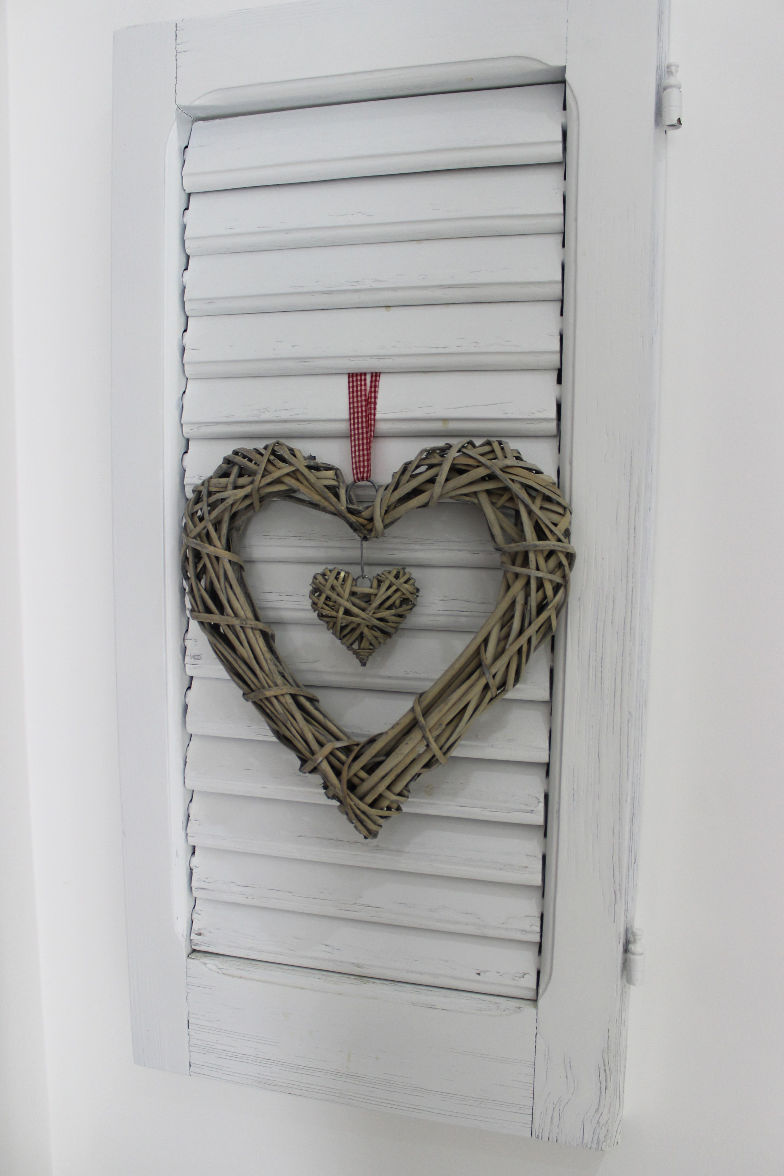 Eine weiße Tür mit horizontaler Holzverkleidung und einem herzförmigen Korbschmuck.
