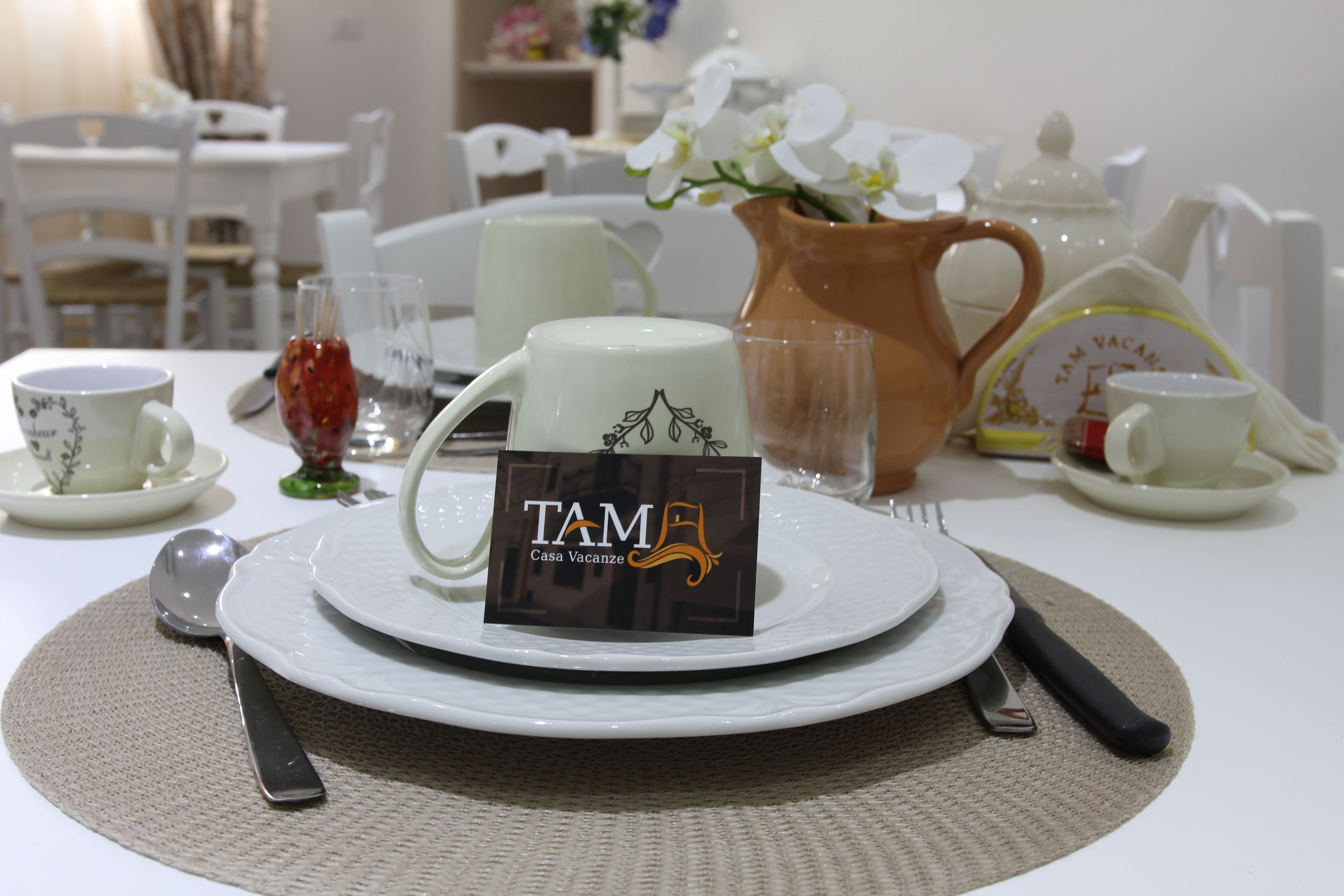 A table set with white plates, a teapot, a pitcher, and a sign reading "TAM Casa Vacanze".