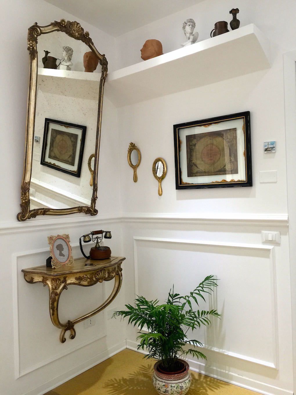 Una habitación con un espejo grande y ornamentado, una mesita con un teléfono y una planta en maceta.