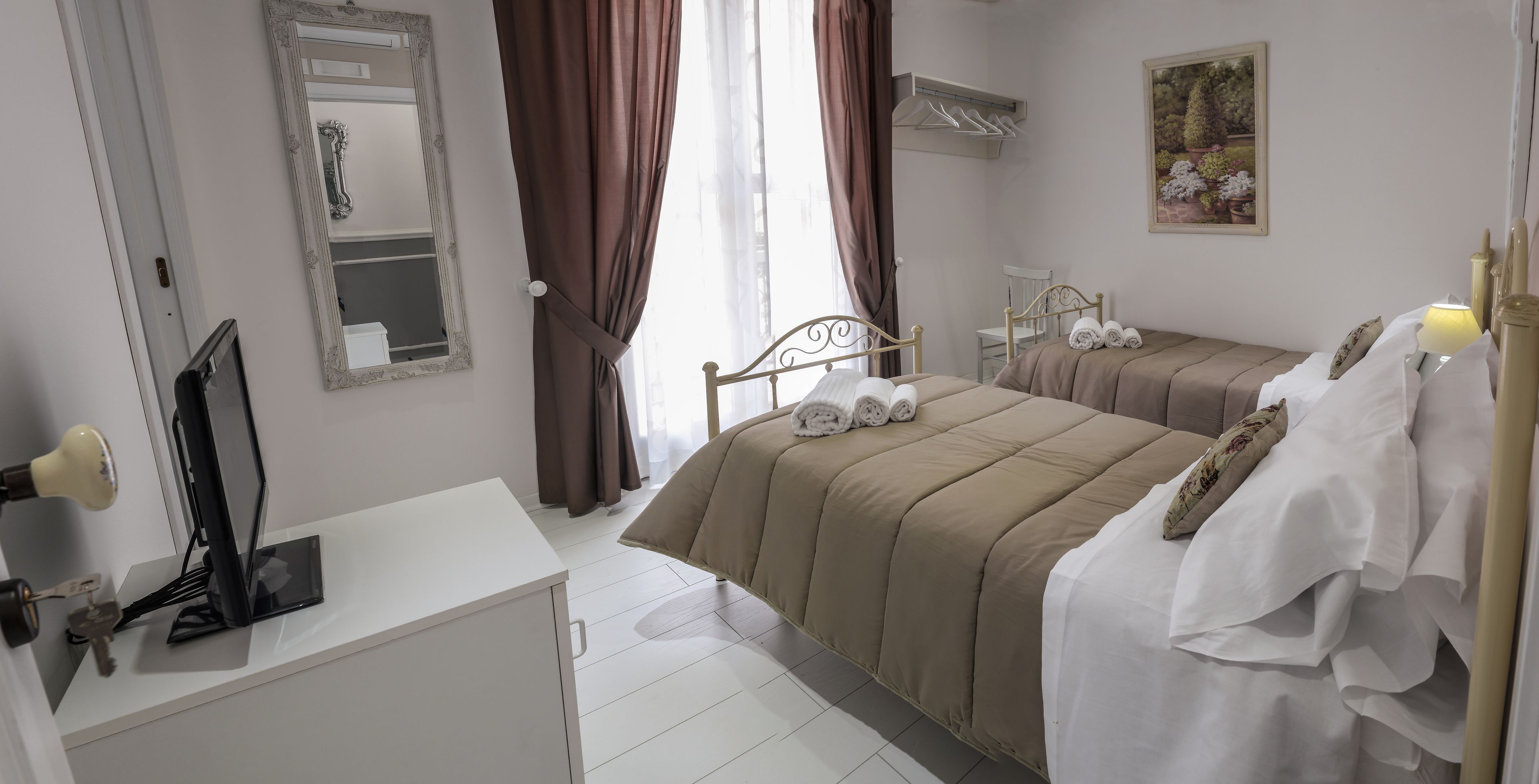 A hotel room with a bed, a desk, a mirror, and a painting on the wall.
