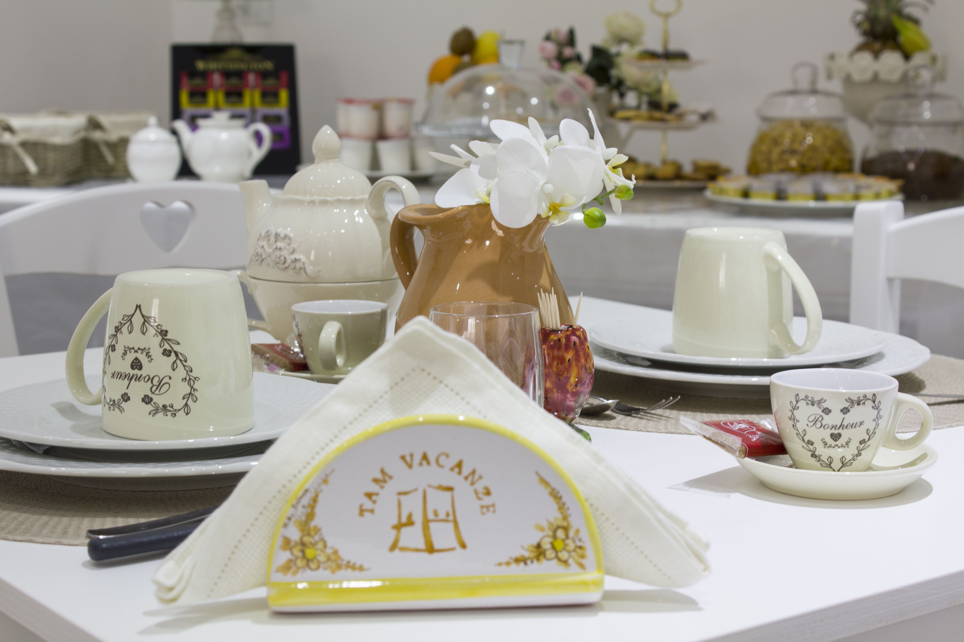 A table set with white ceramic tea sets, including teapots, cups, and saucers, arranged for a tea service.