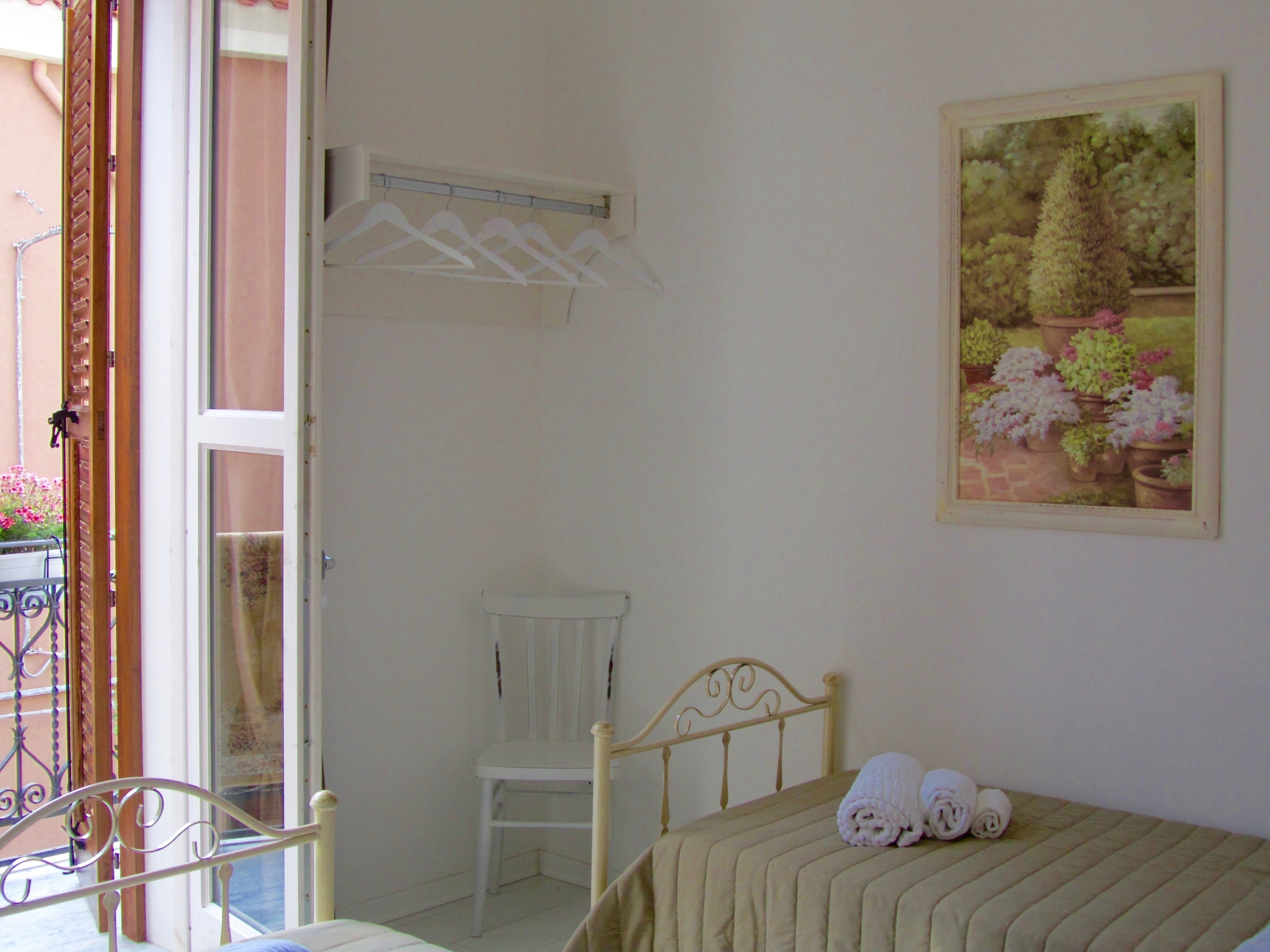 Ein Schlafzimmer mit Bett, Stuhl, einer Kleiderstange und einem Blumenbild.