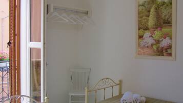 Quarto com cama, uma cadeira, um cabideiro e um quadro de flores.