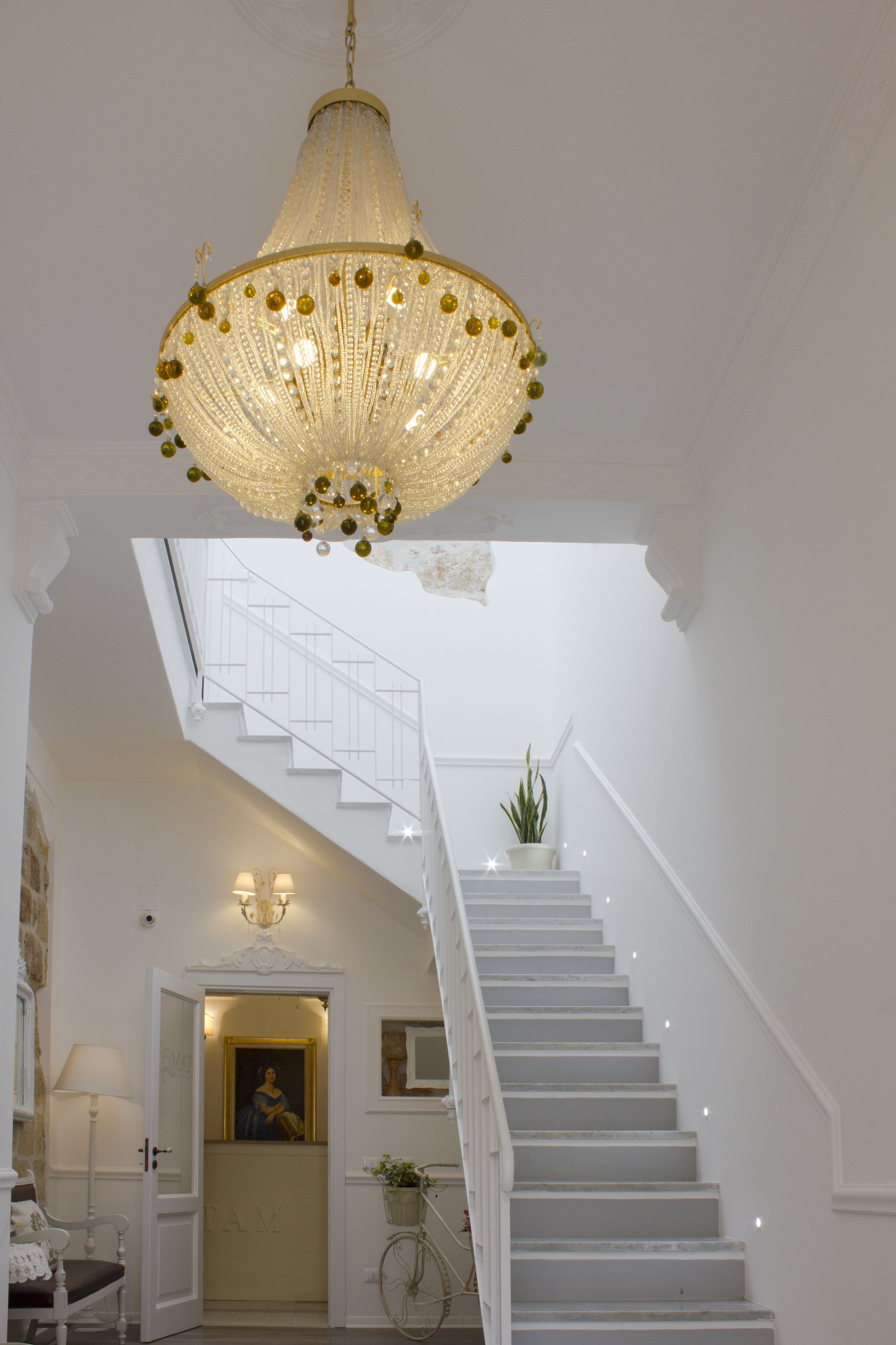 Un escalier aux marches blanches, surmonté d’un lustre.