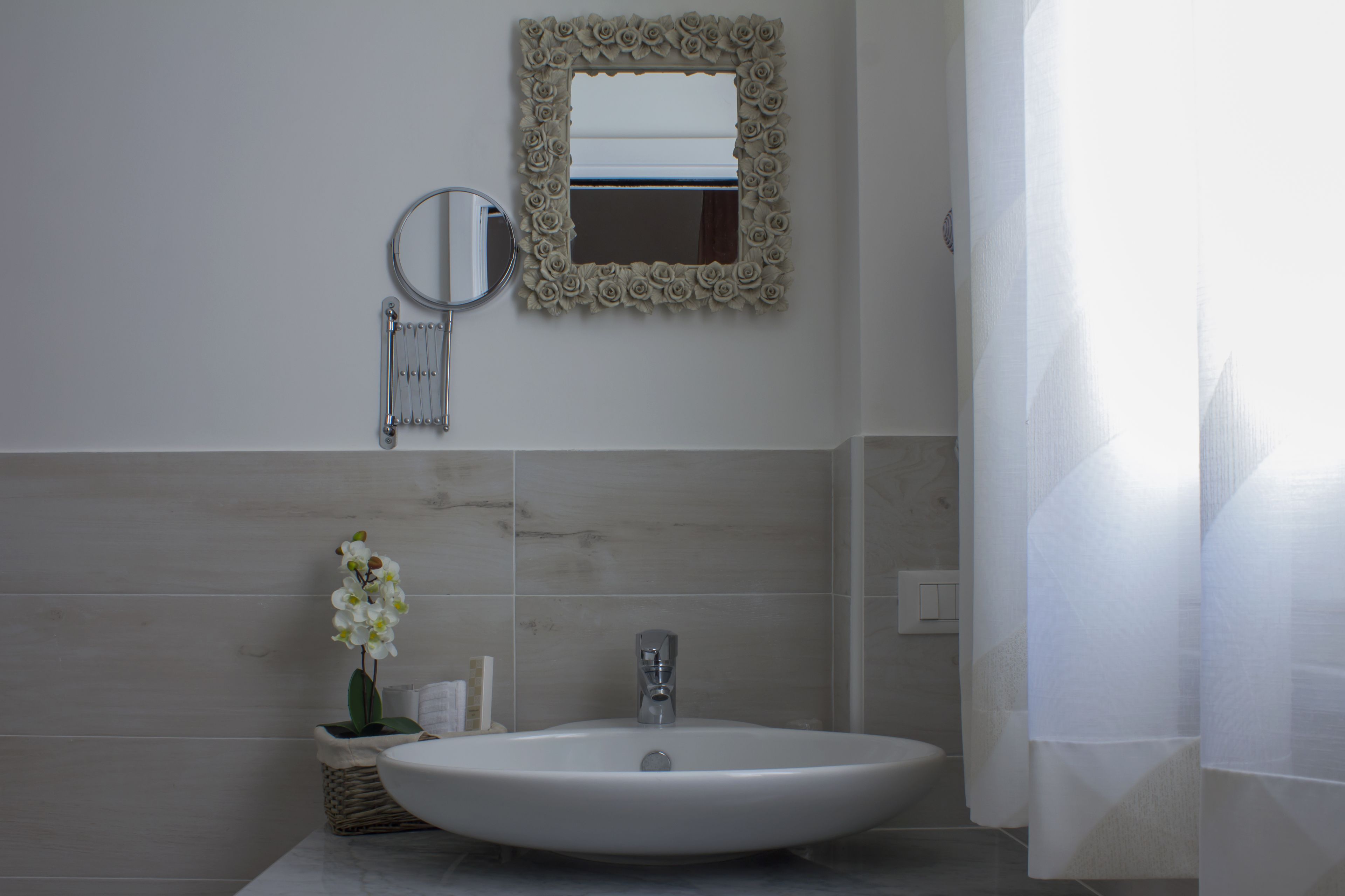 A bathroom with a large oval sink, a mirror with a floral frame, and a small wicker basket with toiletries.