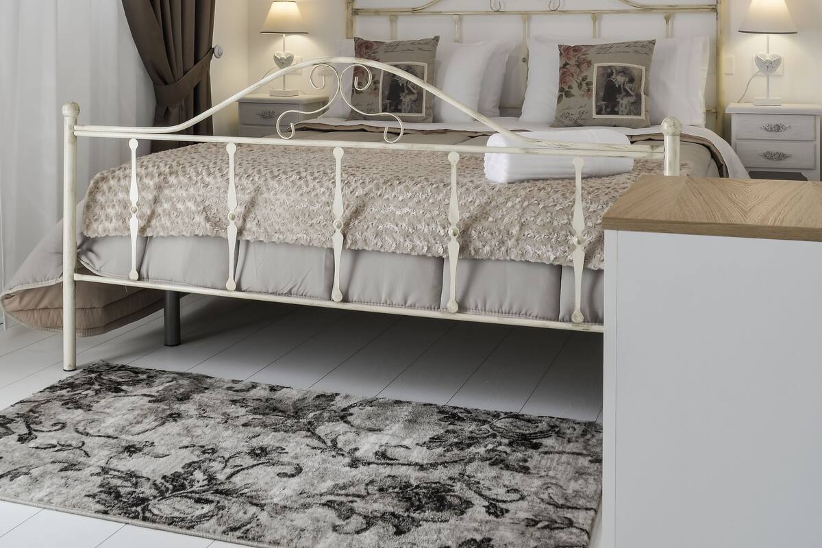 A bedroom with a white metal bed frame, a floral painting on the wall, and a ceiling fan.
