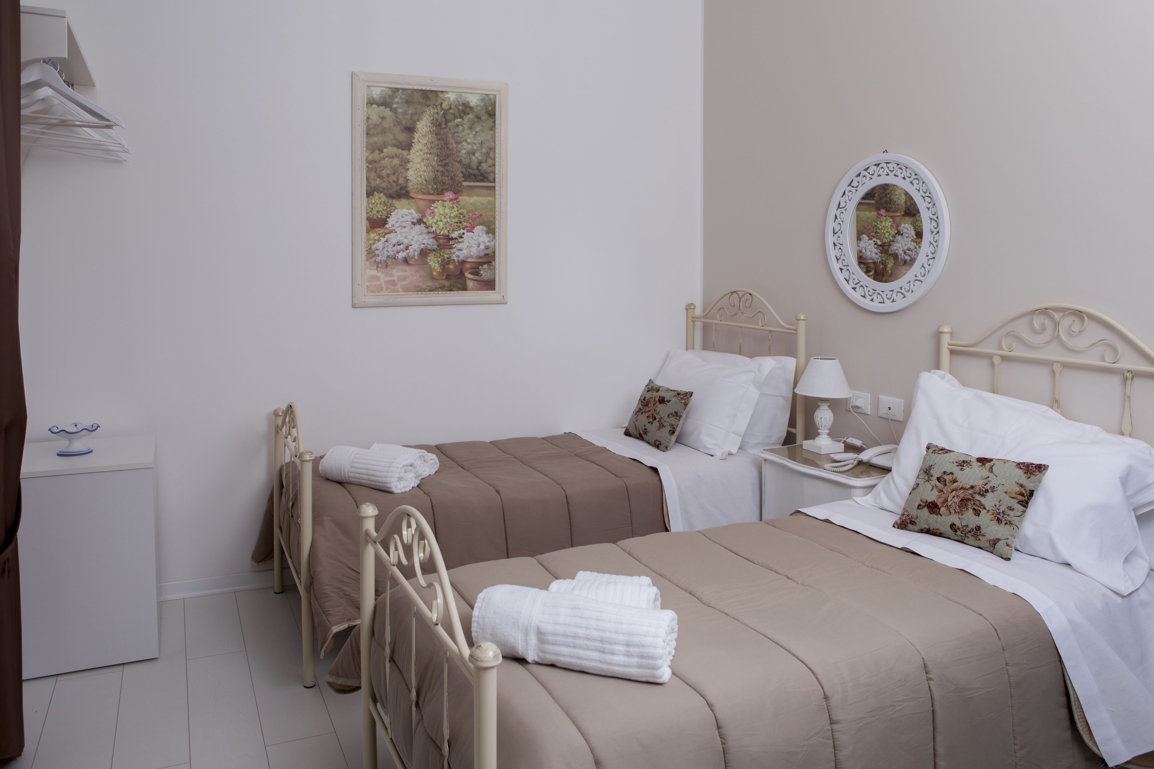 A hotel room with two beds, a bedside table with a lamp, a small bedside table with a phone, and a wall-mounted mirror.