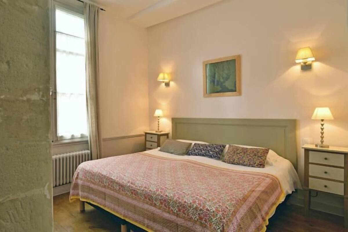 A bedroom with a bed, two bedside tables, a radiator, and a window with curtains.