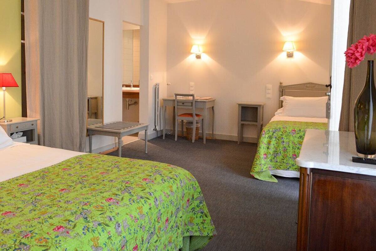 A hotel room with two beds, a desk, a chair, a mirror, and a vase with flowers.