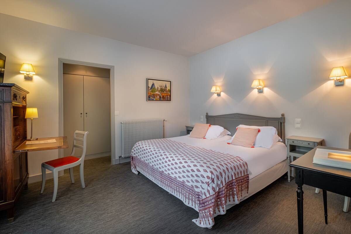 A bedroom with a bed, bedside tables, a chair, a desk, and a radiator.