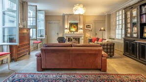 Ein Wohnzimmer mit braunem Sofa, Kamin, Bücherregal und einem gemusterten Teppich.