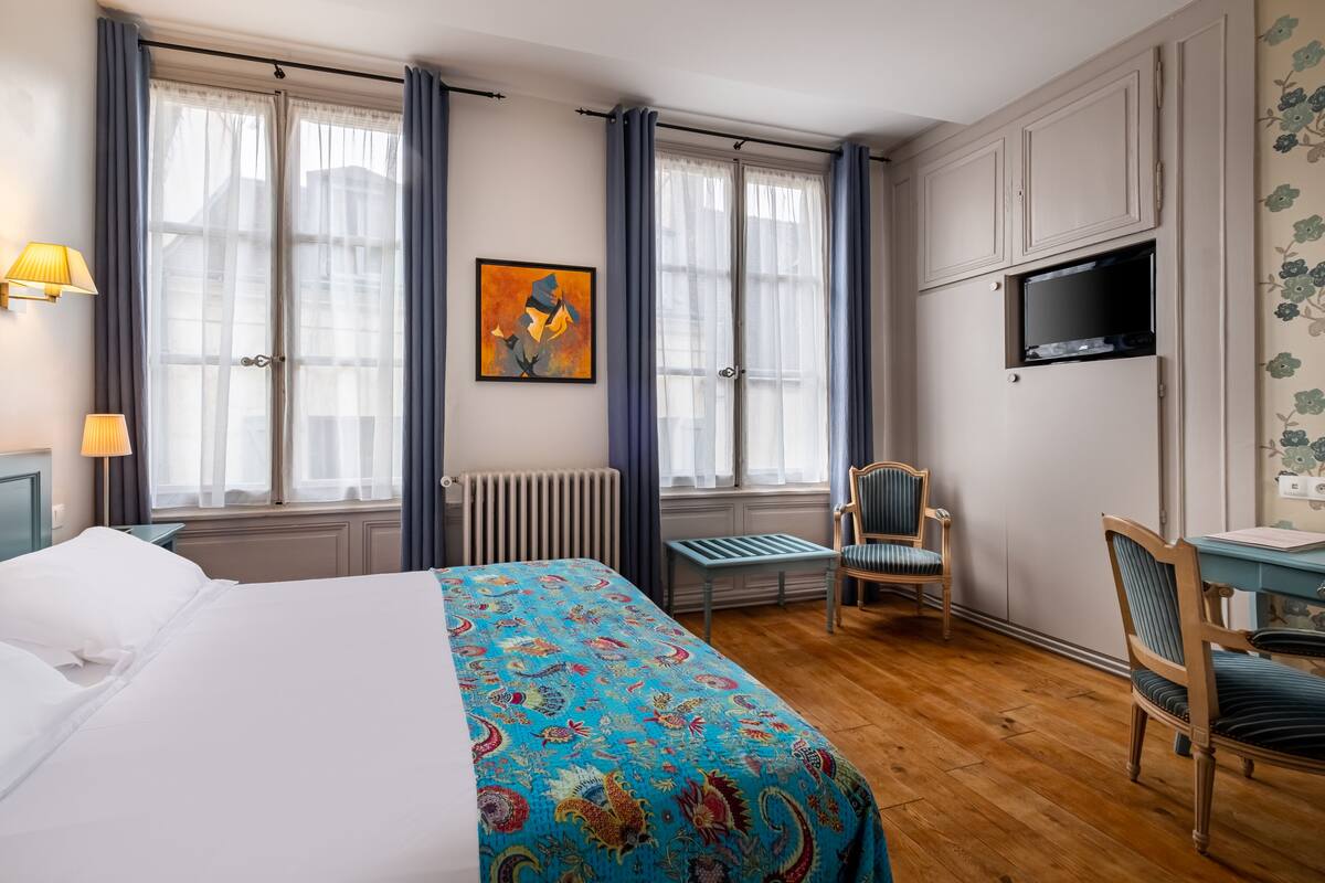 A hotel room with a bed, a desk, a chair, a TV, and a window with curtains.
