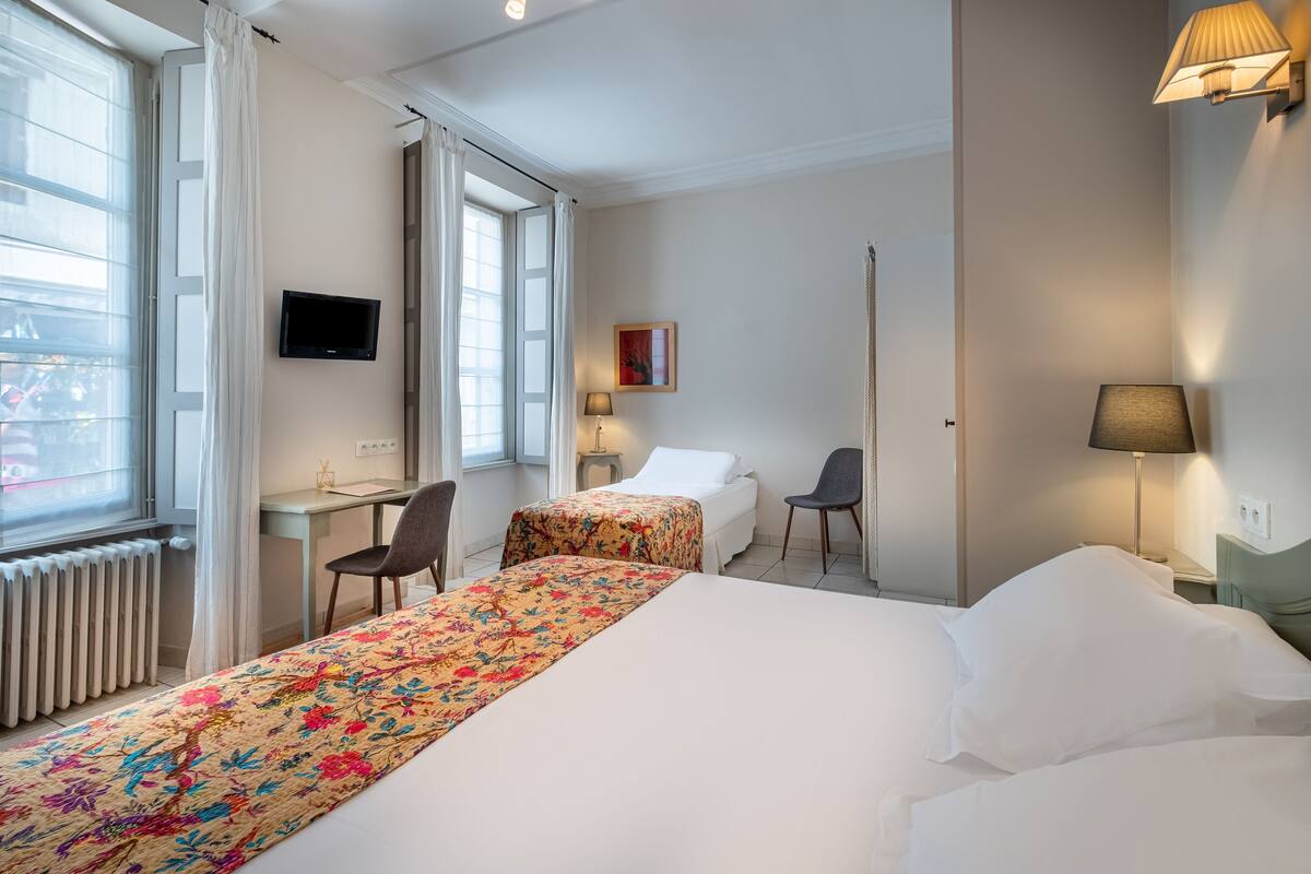 A hotel room with two beds, a desk, a chair, a TV, and a window with curtains.