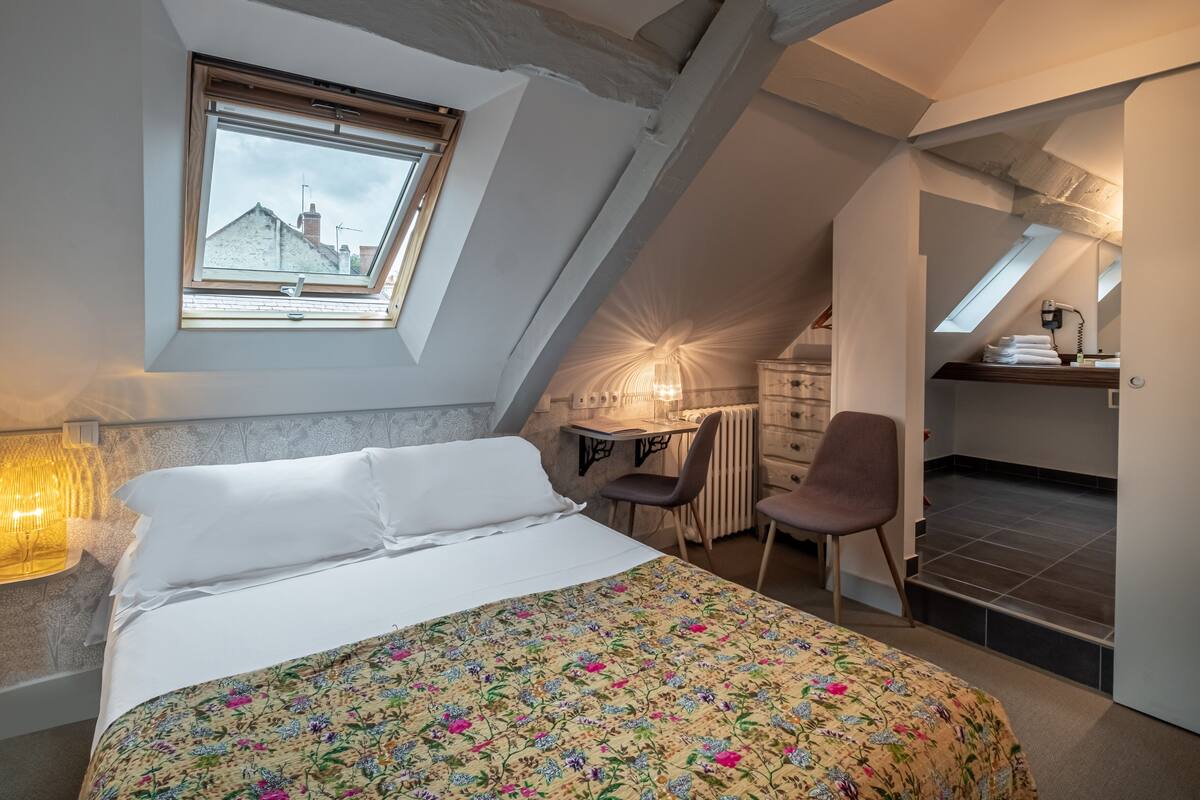 A bedroom with a bed, a desk, a chair, and a radiator.