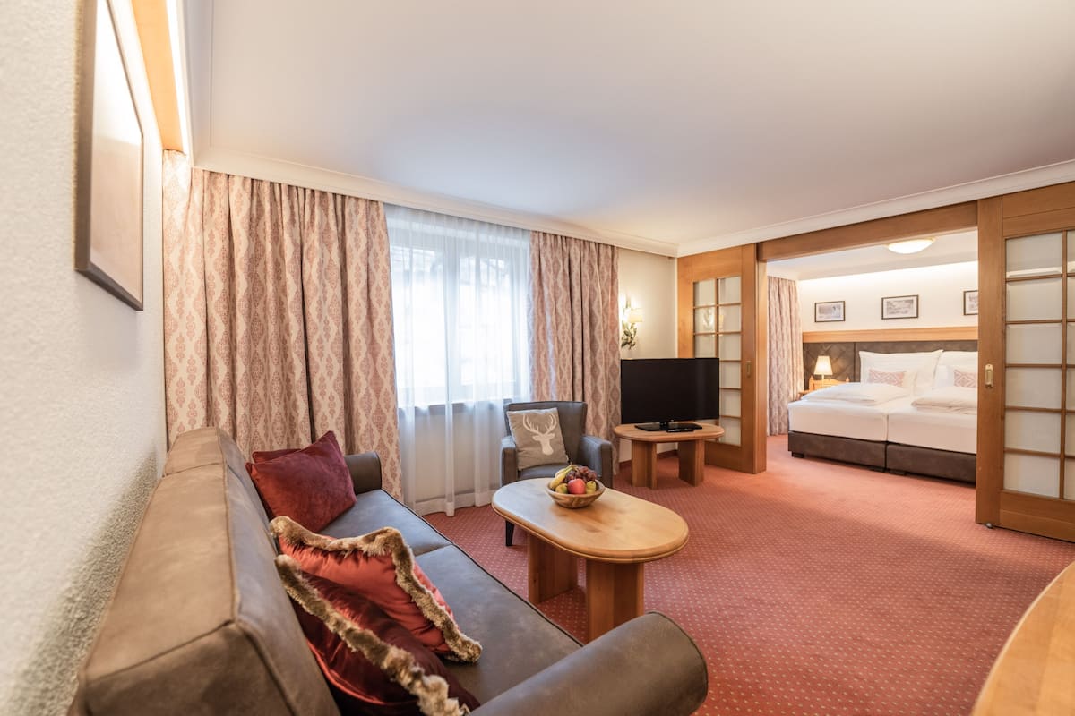 Ett hotellrum med en soffa, ett litet bord med en fruktskål, en TV och en säng med utsikt genom en skjutdörr.