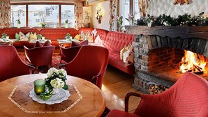 A cozy room with a fireplace, red seating, and a view of the city through large windows. - Hotel Ulli (Lech am Arlberg)