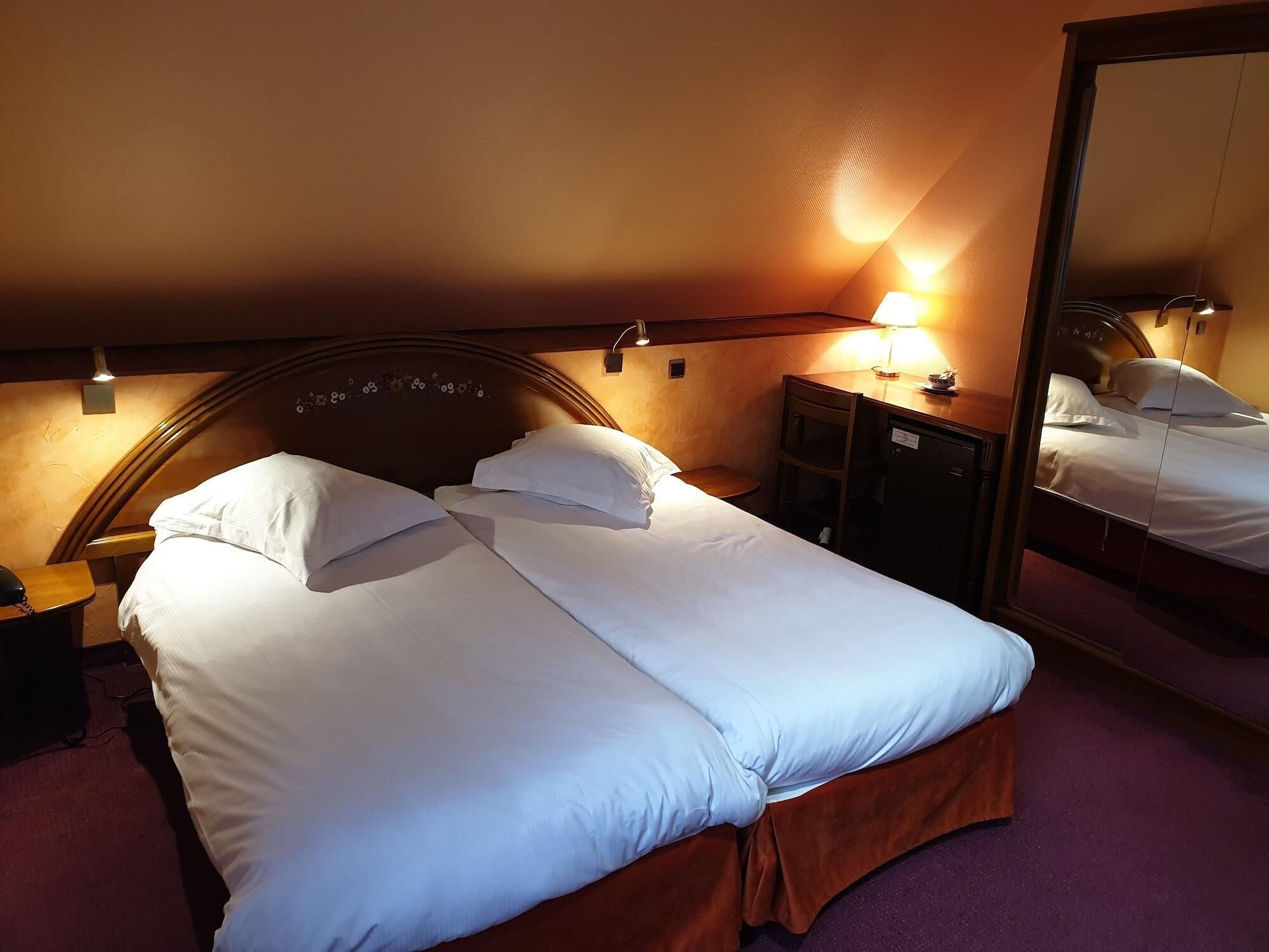Un letto rifatto con lenzuola bianche, una testiera in legno, un comodino con una lampada e uno specchio che riflette il letto.