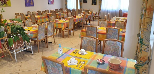 A dining area with multiple tables set with chairs, each table covered with a colorful tablecloth. - Hotel Restaurant le Faudé (Lapoutroie)