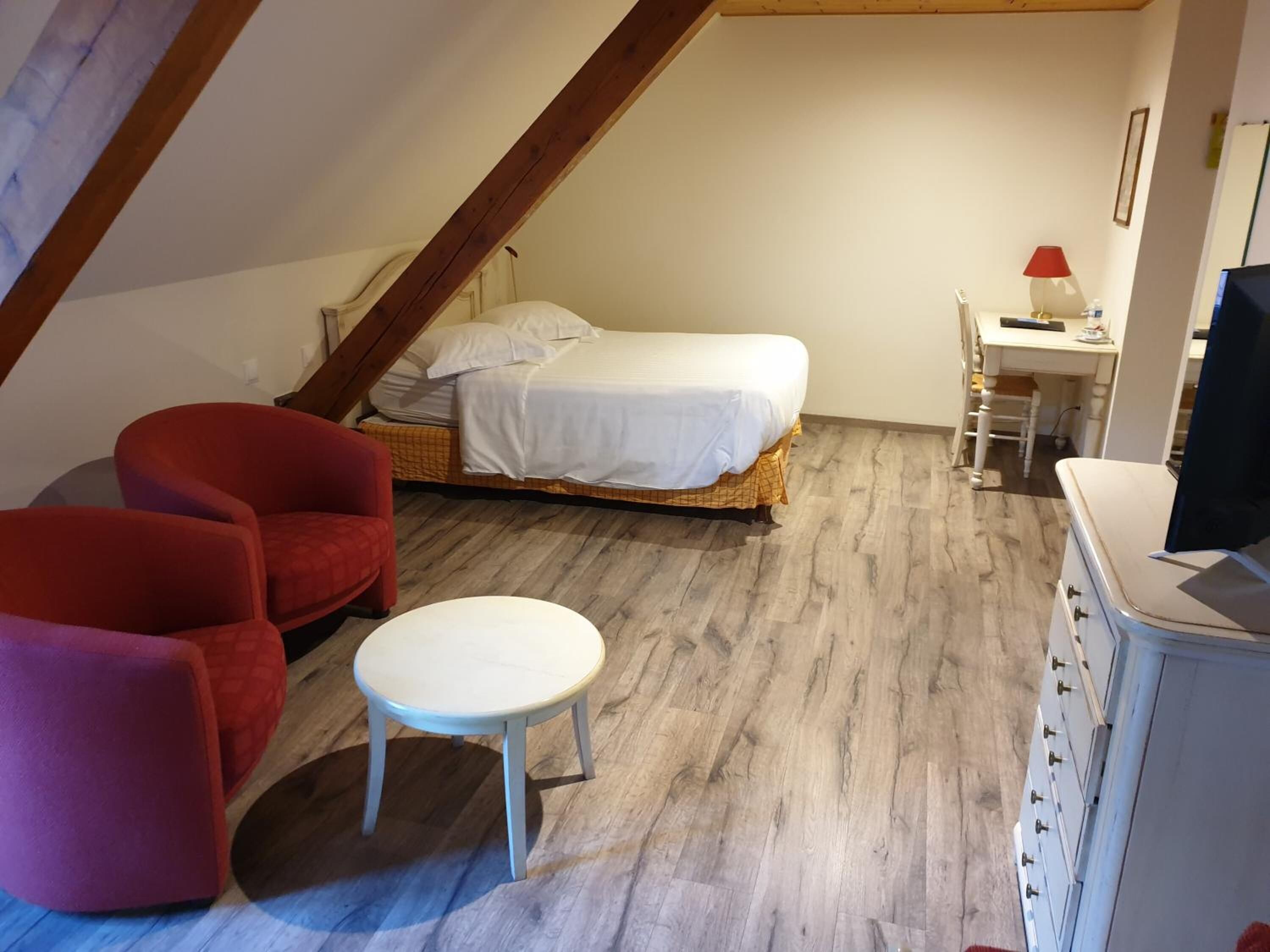 A small, cozy room with a loft bed, a red armchair, a white table, and a dresser.