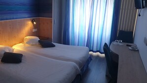 Ein Hotelzimmer mit zwei Betten, einem Holzkopfteil, einem an der Wand befestigten Fernseher und einem Fenster mit Vorhängen.