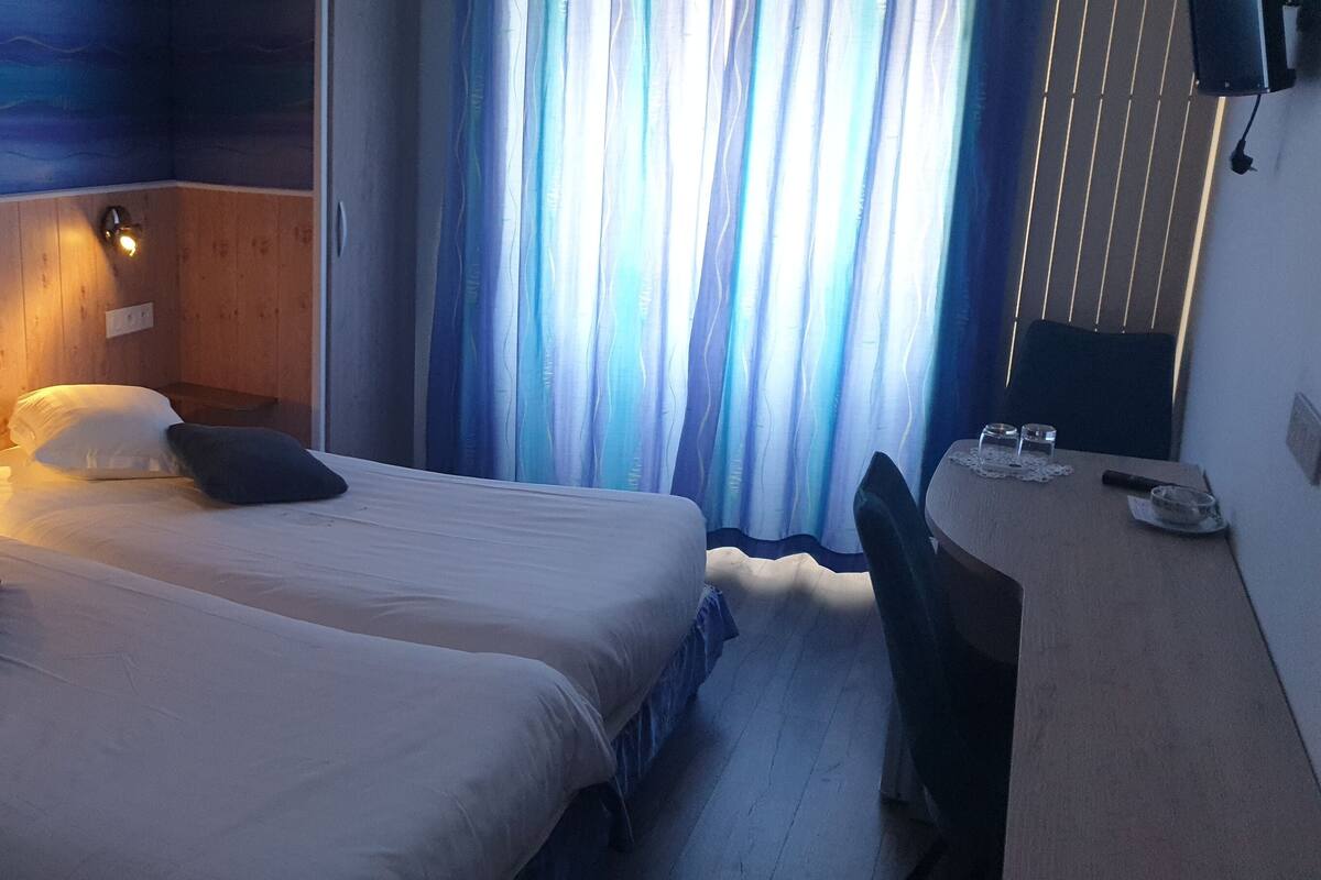 Een hotelkamer met twee bedden, een houten hoofdbord, een wandtelevisie en een raam met gordijnen.