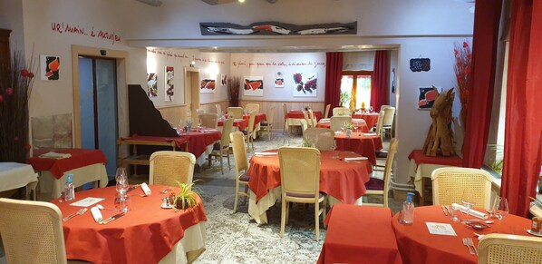 A restaurant with tables set for dining, wicker chairs, and red tablecloths.