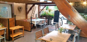 Ein Straßencafé mit Holztischen und -stühlen, einer Kreidetafel mit Speisekarte und Blumentöpfen.