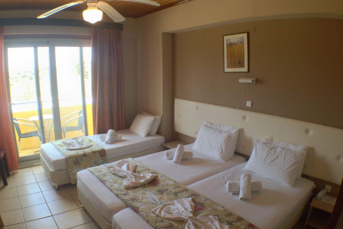 A hotel room with two beds, a ceiling fan, and a view of the outdoors through a sliding door.